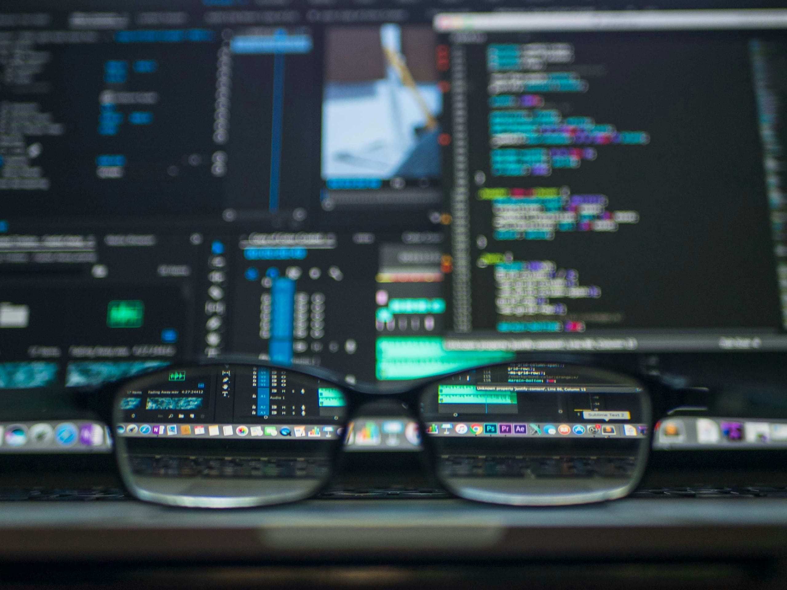 Code and editing timelines on screen, seen through a pair of glasses